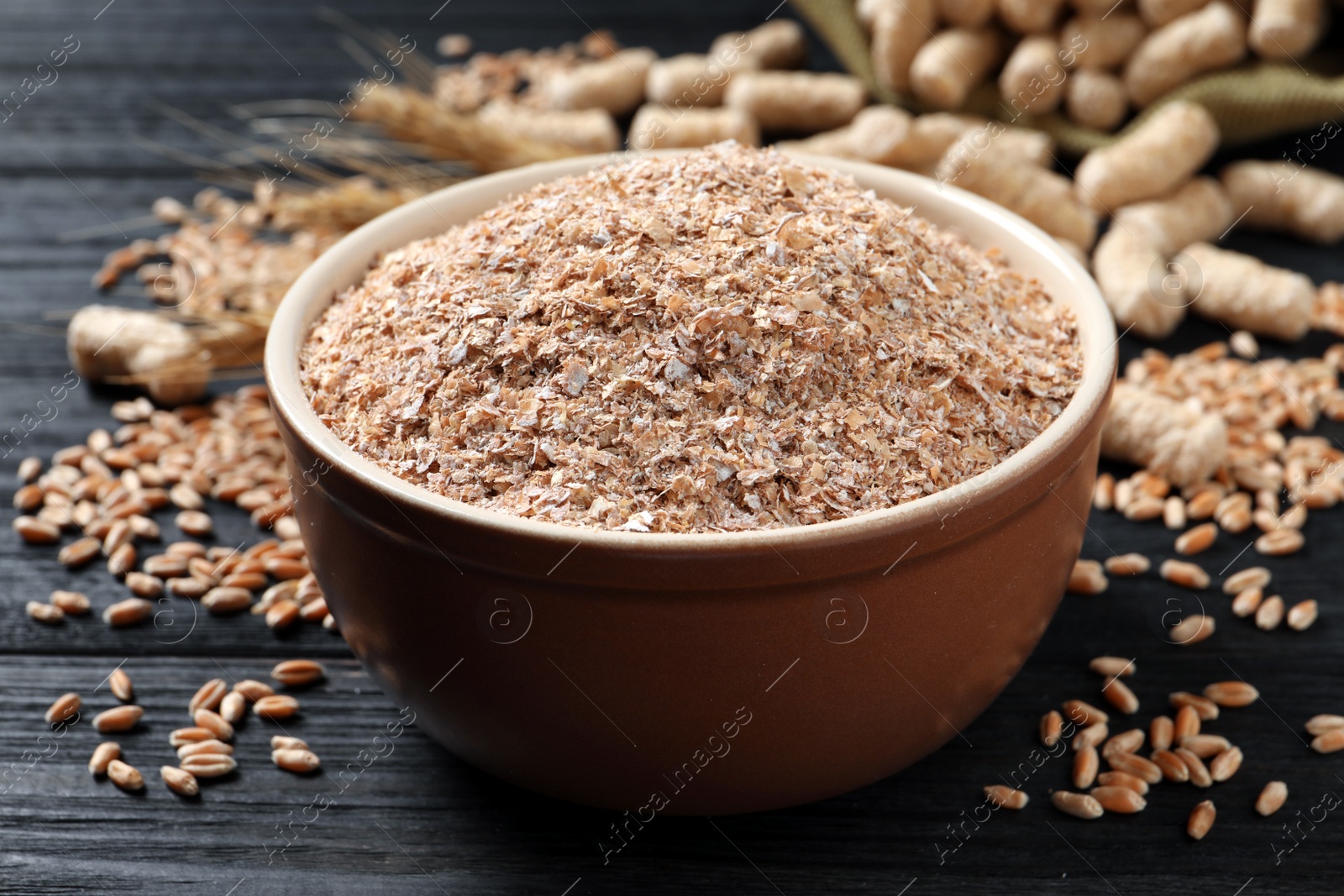 Photo of Bowl of wheat bran on black wooden table