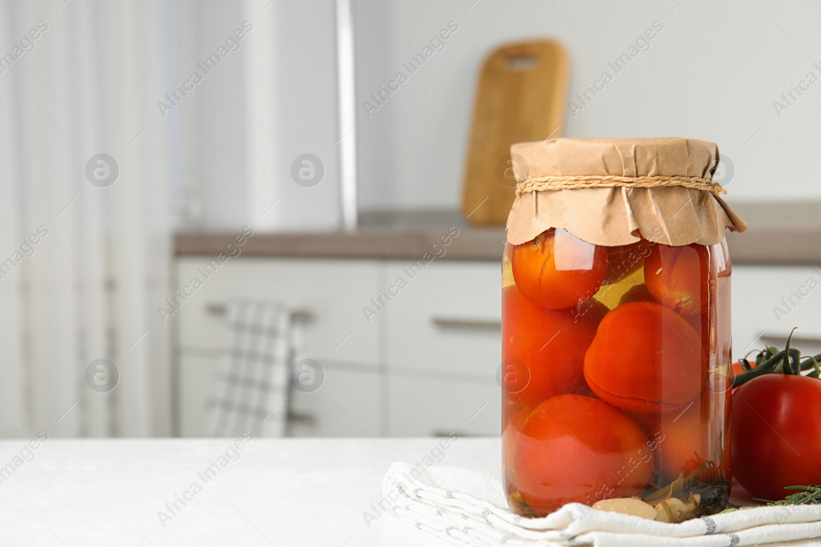 Photo of Pickled tomatoes in glass jar on white table in kitchen, space for text