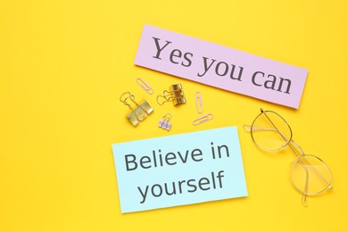 Photo of Notes with motivational quotes, glasses and office stationery on yellow background, flat lay