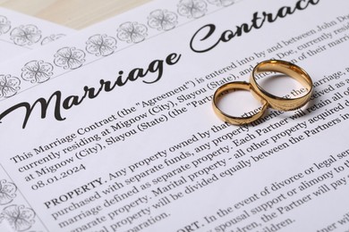 Marriage contracts and gold rings on light wooden table, closeup