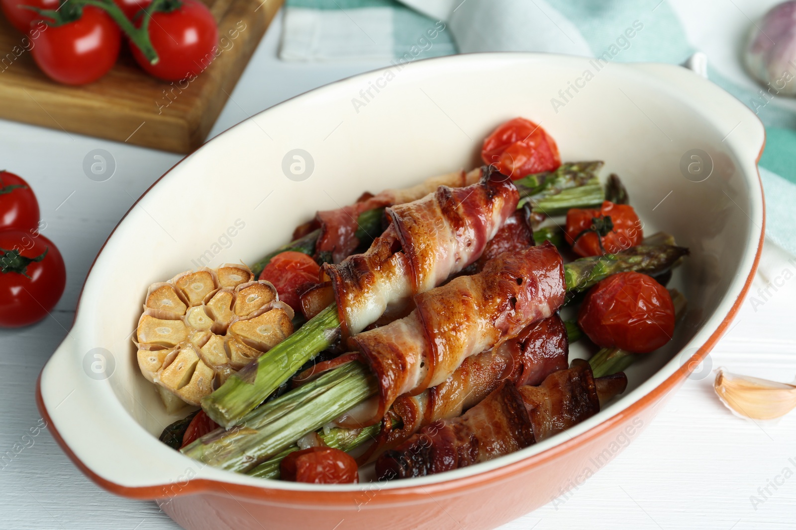 Photo of Oven baked asparagus wrapped with bacon in ceramic dish on white wooden table