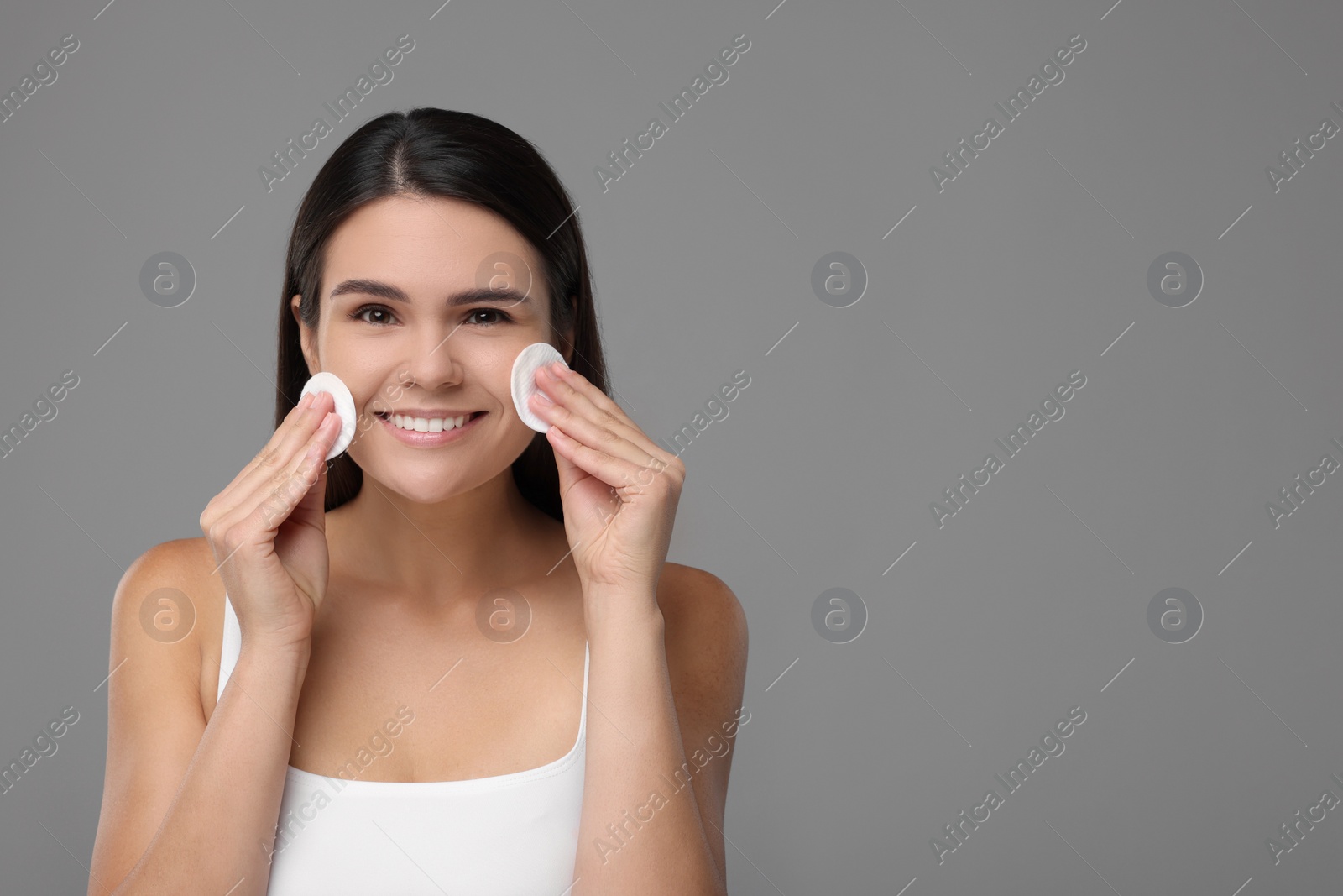 Photo of Young woman cleaning her face with cotton pads on grey background. Space for text