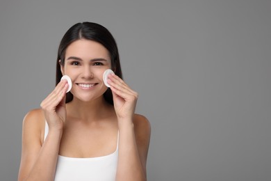 Young woman cleaning her face with cotton pads on grey background. Space for text