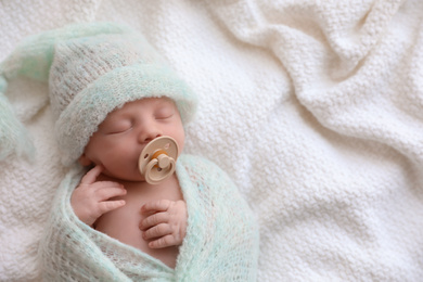 Photo of Cute newborn baby in warm hat sleeping on white plaid, top view. Space for text