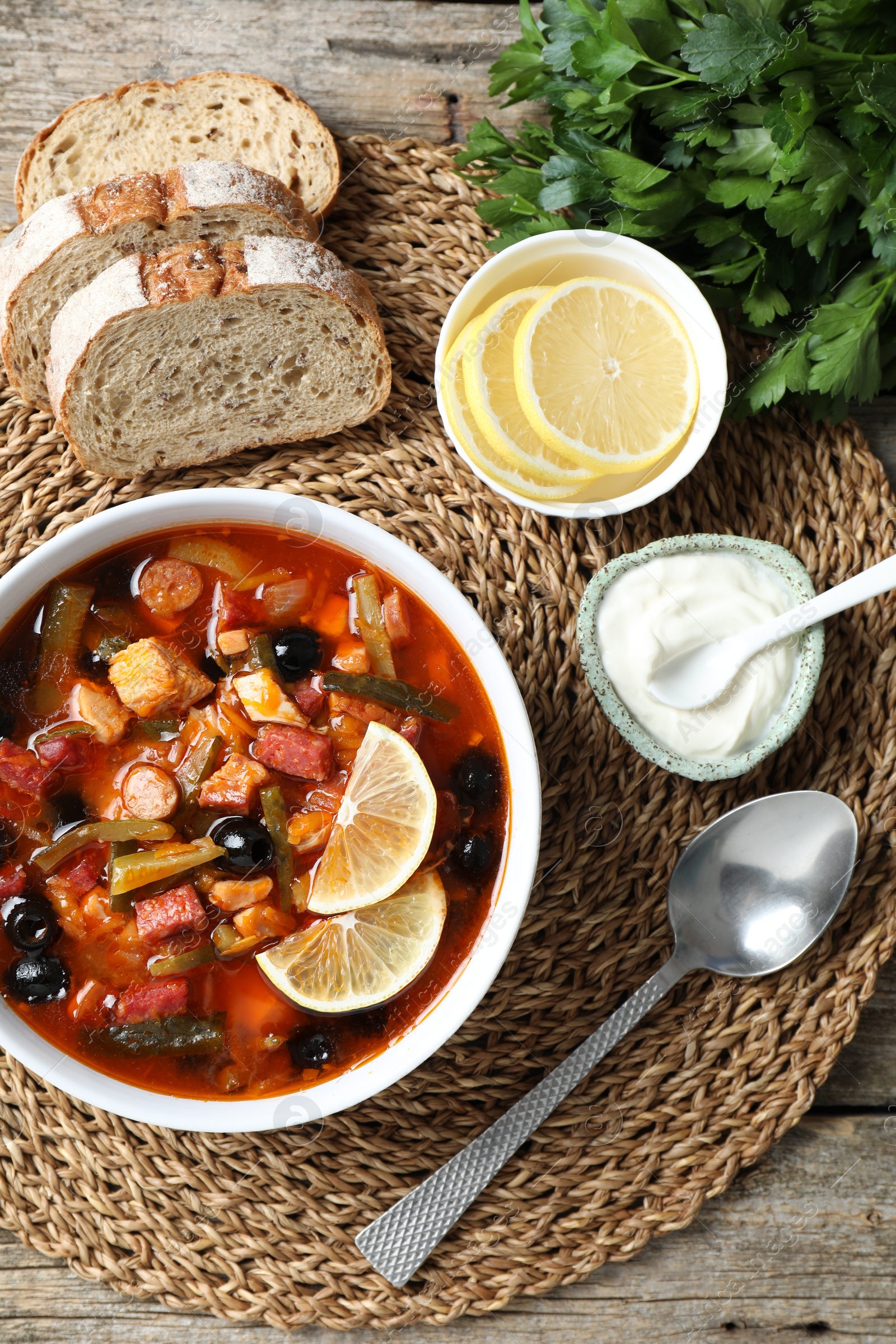 Photo of Meat solyanka soup with sausages, olives and vegetables served on wooden table, flat lay