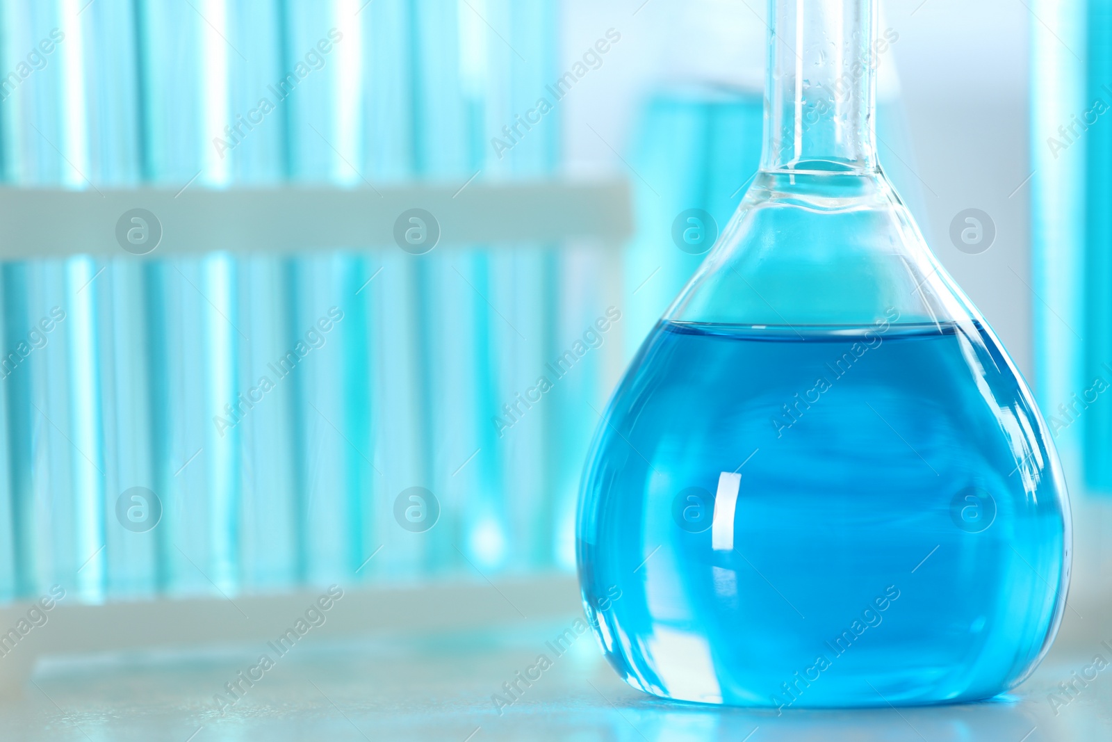 Photo of Volumetric flask with light blue liquid on table, closeup. Space for text