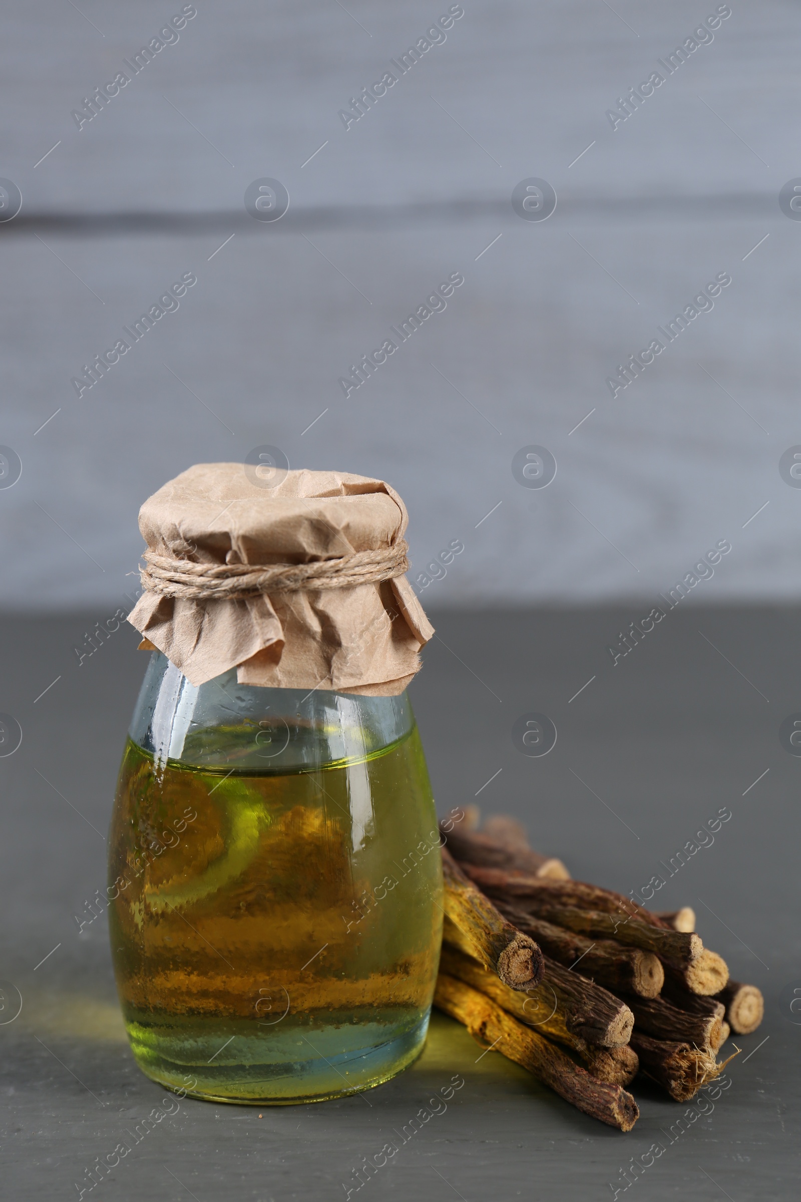 Photo of Dried sticks of licorice roots and essential oil on grey wooden table