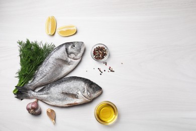 Photo of Raw dorado fish, spices, lemon and oil on white wooden table, flat lay. Space for text