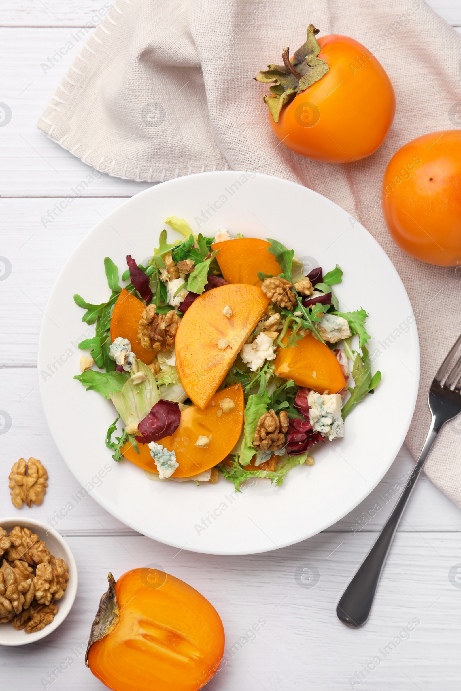 Photo of Delicious persimmon salad and fork on white wooden table, flat lay