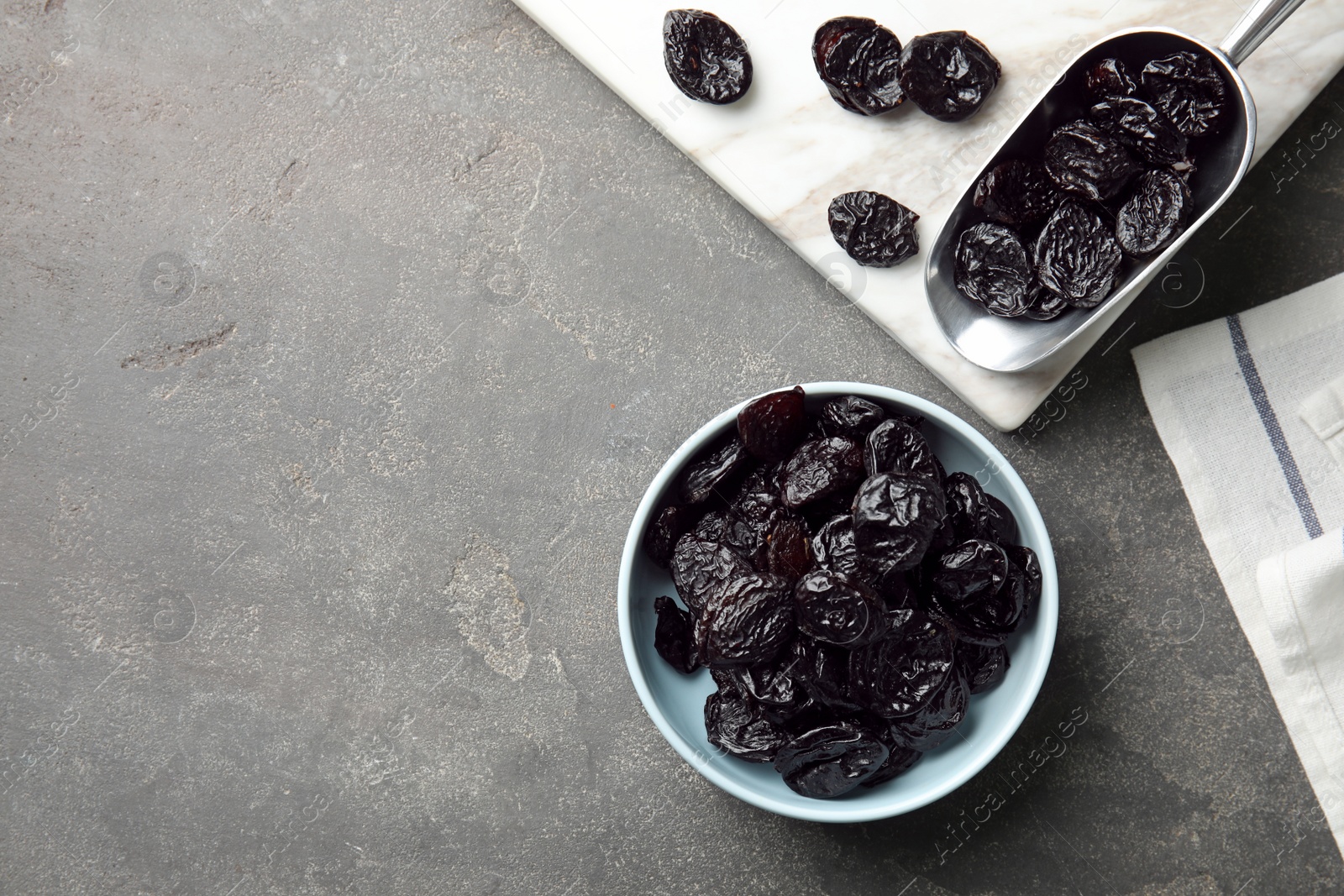 Photo of Bowl and scoop of sweet dried plums on table, top view with space for text. Healthy fruit