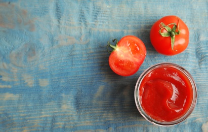 Jar with homemade tomato sauce, fresh vegetables and space for text on wooden table, top view