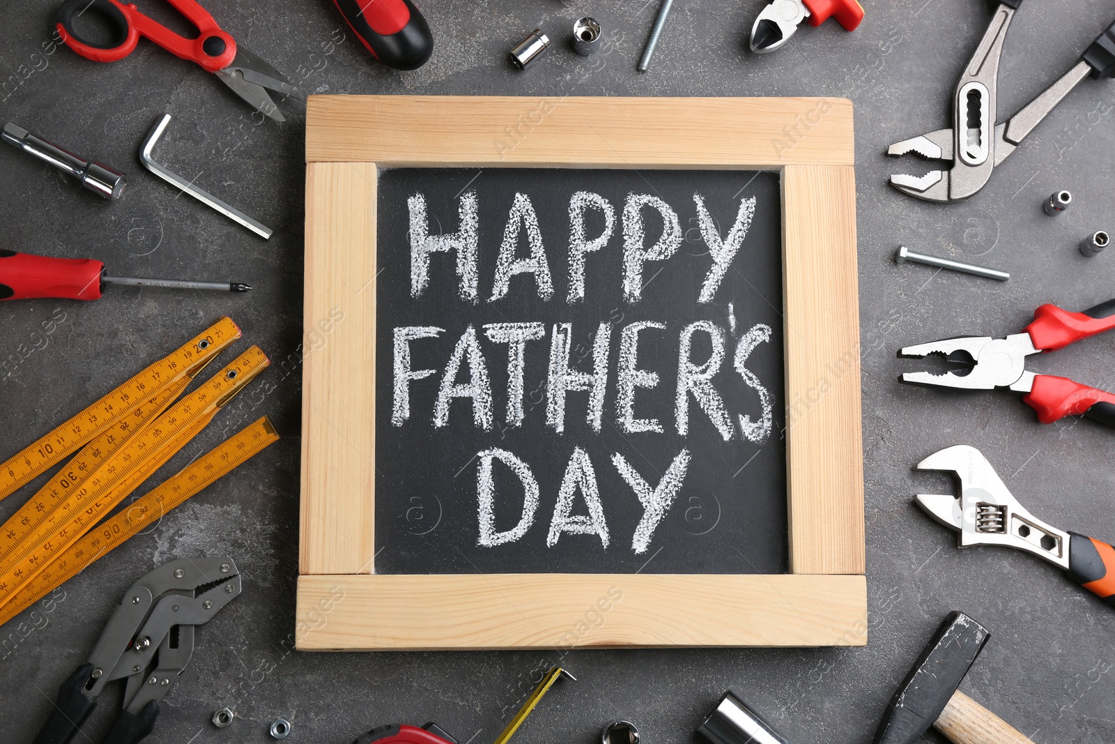 Photo of Blackboard with words HAPPY FATHER'S DAY and tools on grey stone background, flat lay