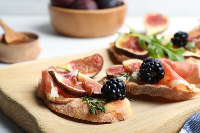 Photo of Sandwiches with ripe figs and prosciutto served on wooden board, closeup