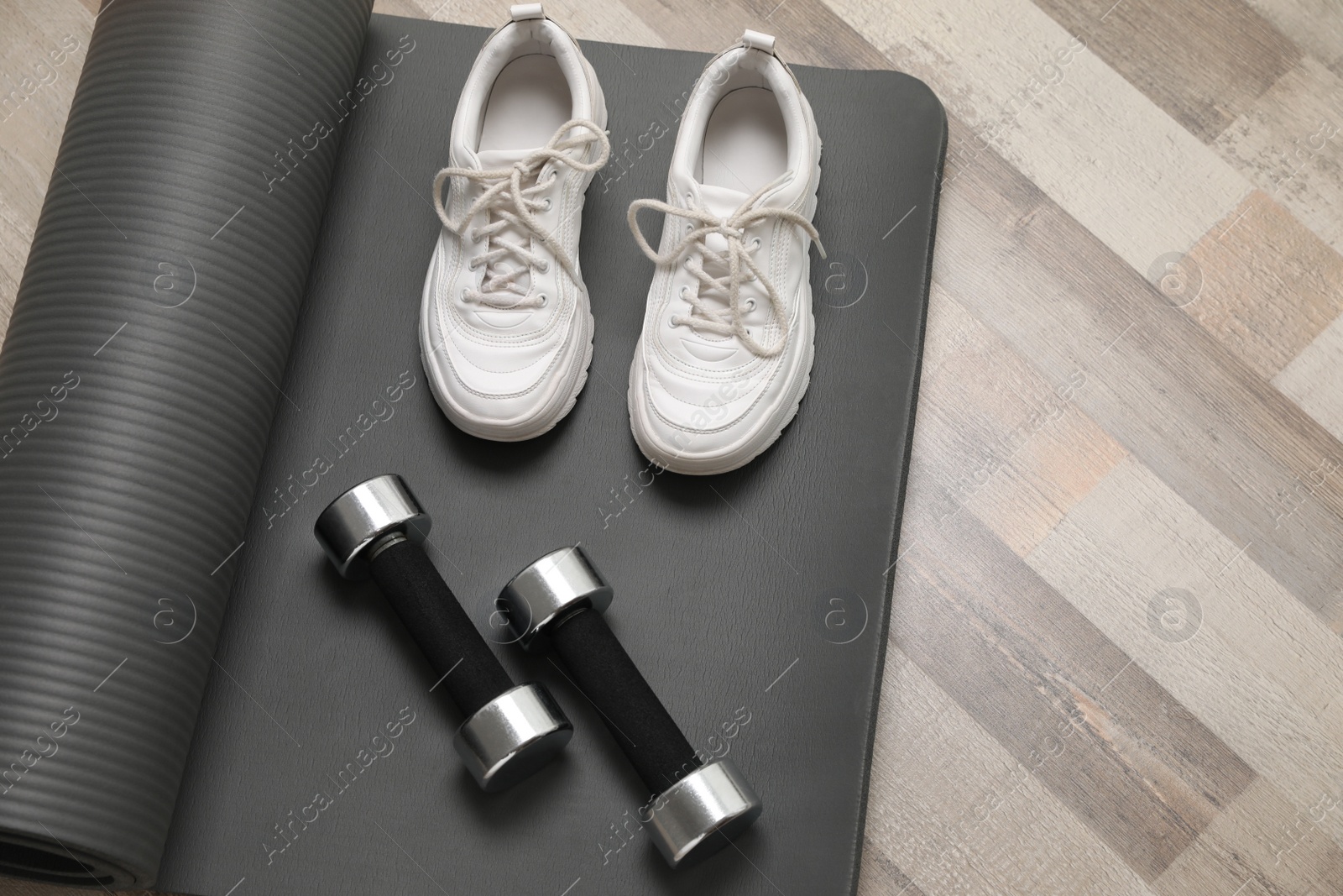 Photo of Dumbbells, sneakers and mat on wooden floor, above view