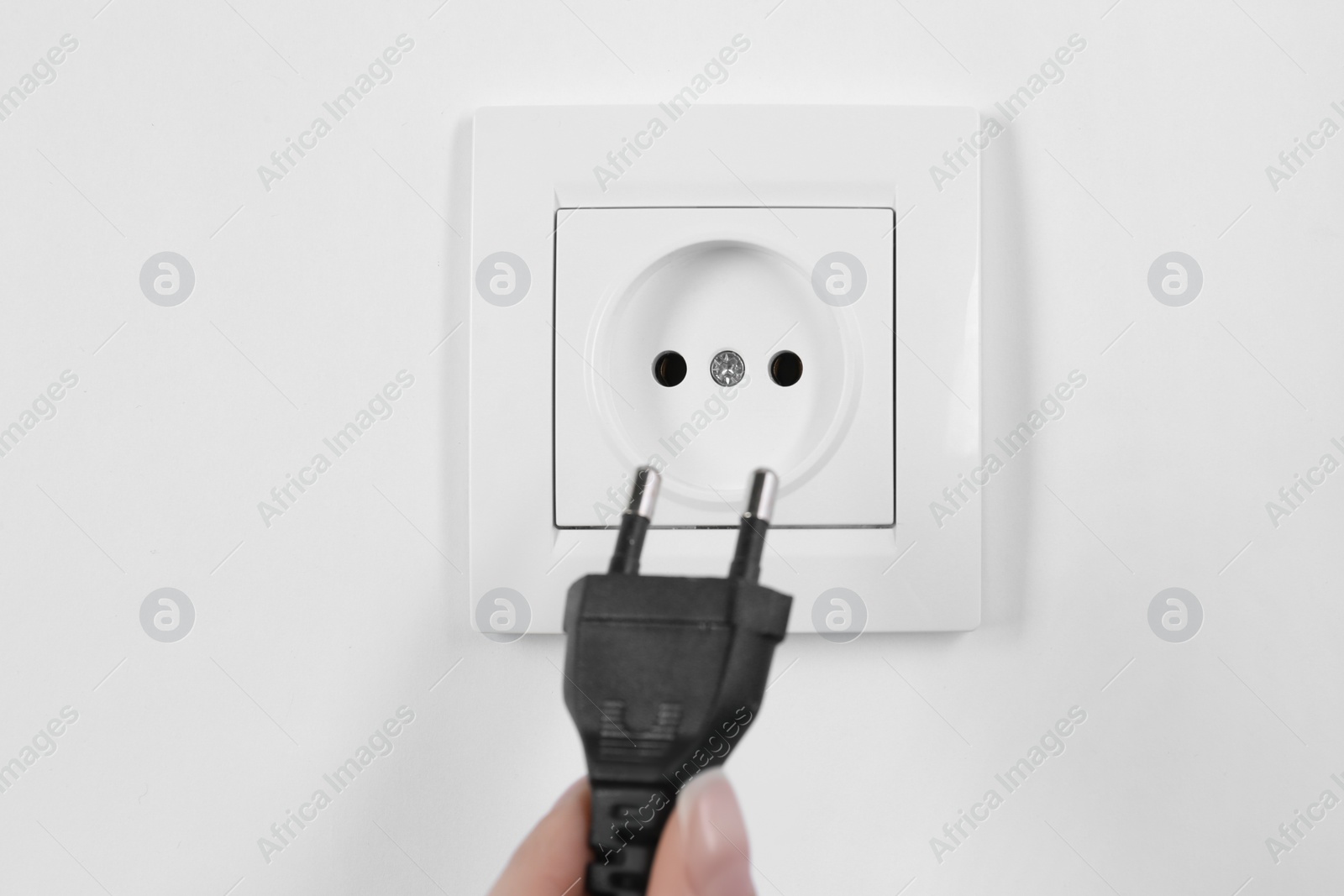 Photo of Woman putting plug into power socket on white background, closeup. Electrician's equipment