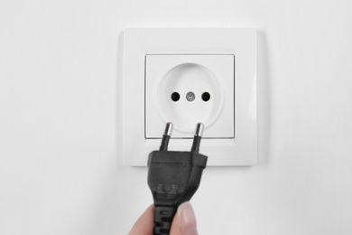 Woman putting plug into power socket on white background, closeup. Electrician's equipment