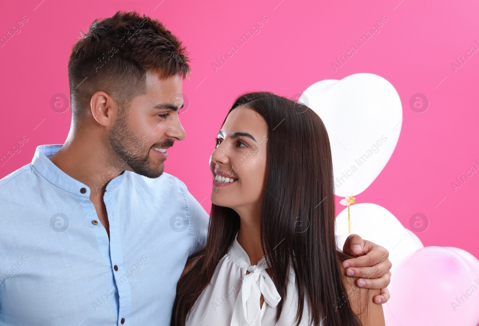 Photo of Young couple and air balloons on pink background. Celebration of Saint Valentine's Day