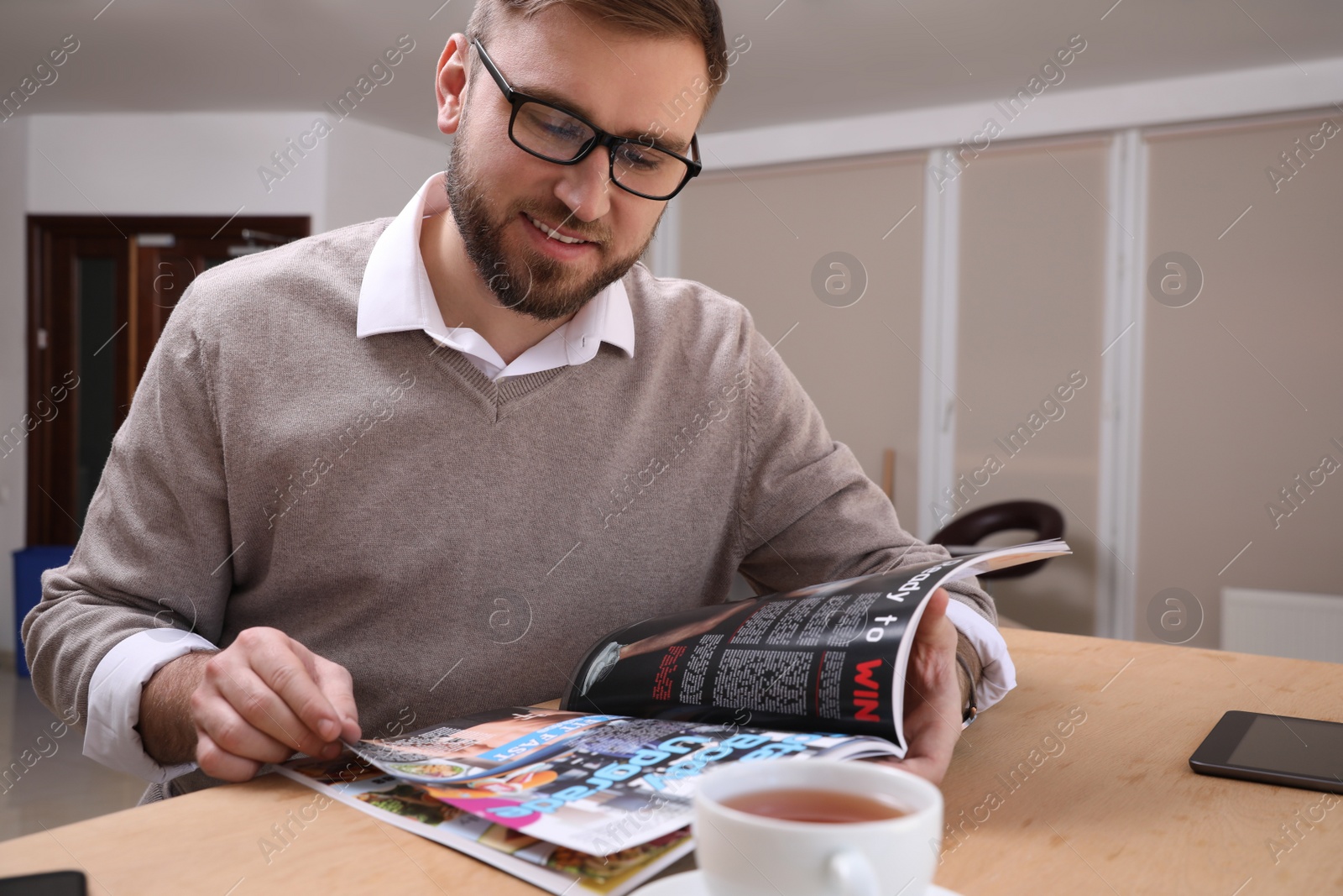 Photo of Young man reading sports magazine at table indoors