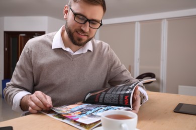 Young man reading sports magazine at table indoors