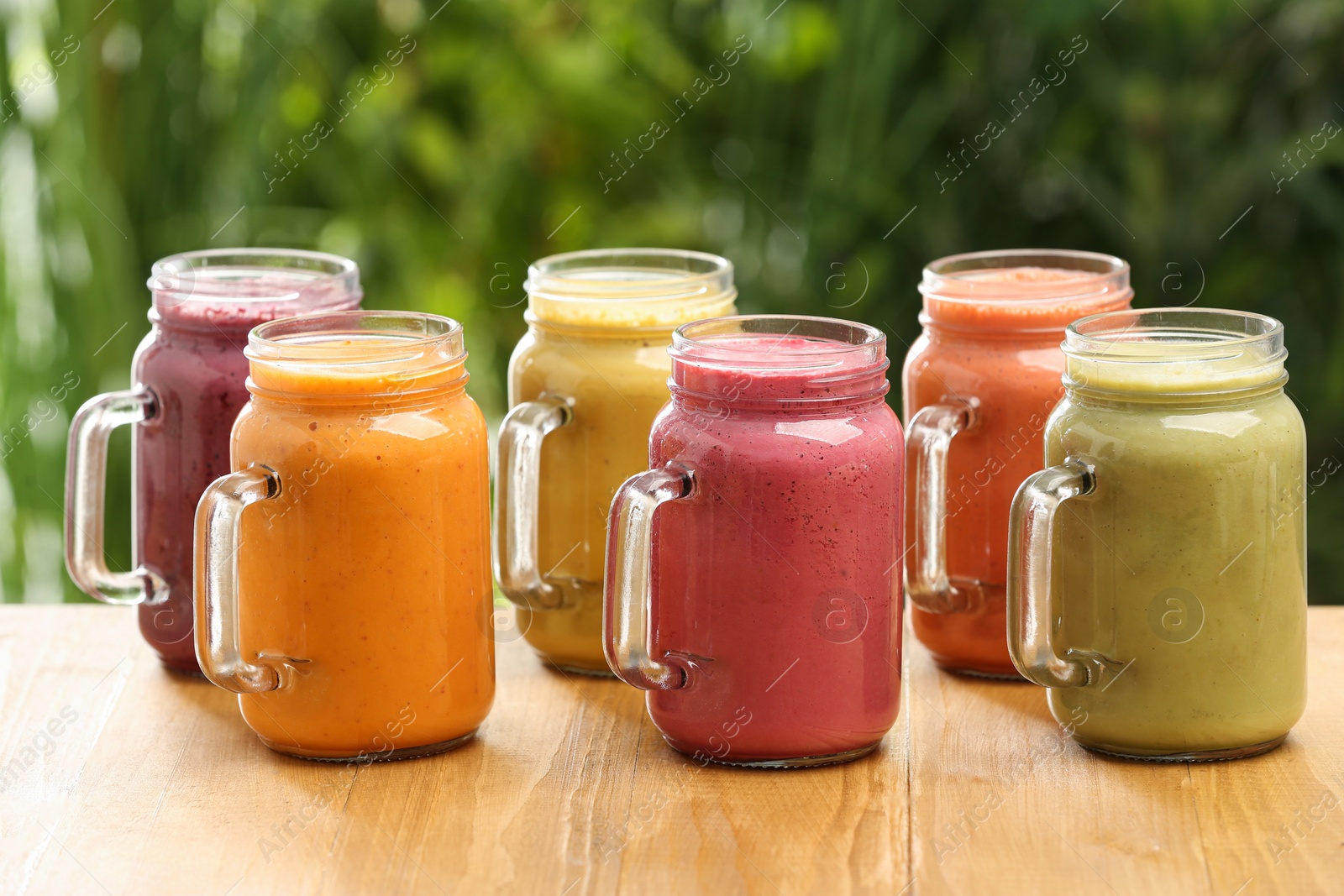 Photo of Many different delicious smoothies in mason jars on wooden table against blurred background