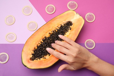 Photo of Young woman touching half of papaya and condoms on color background, top view. Sex concept