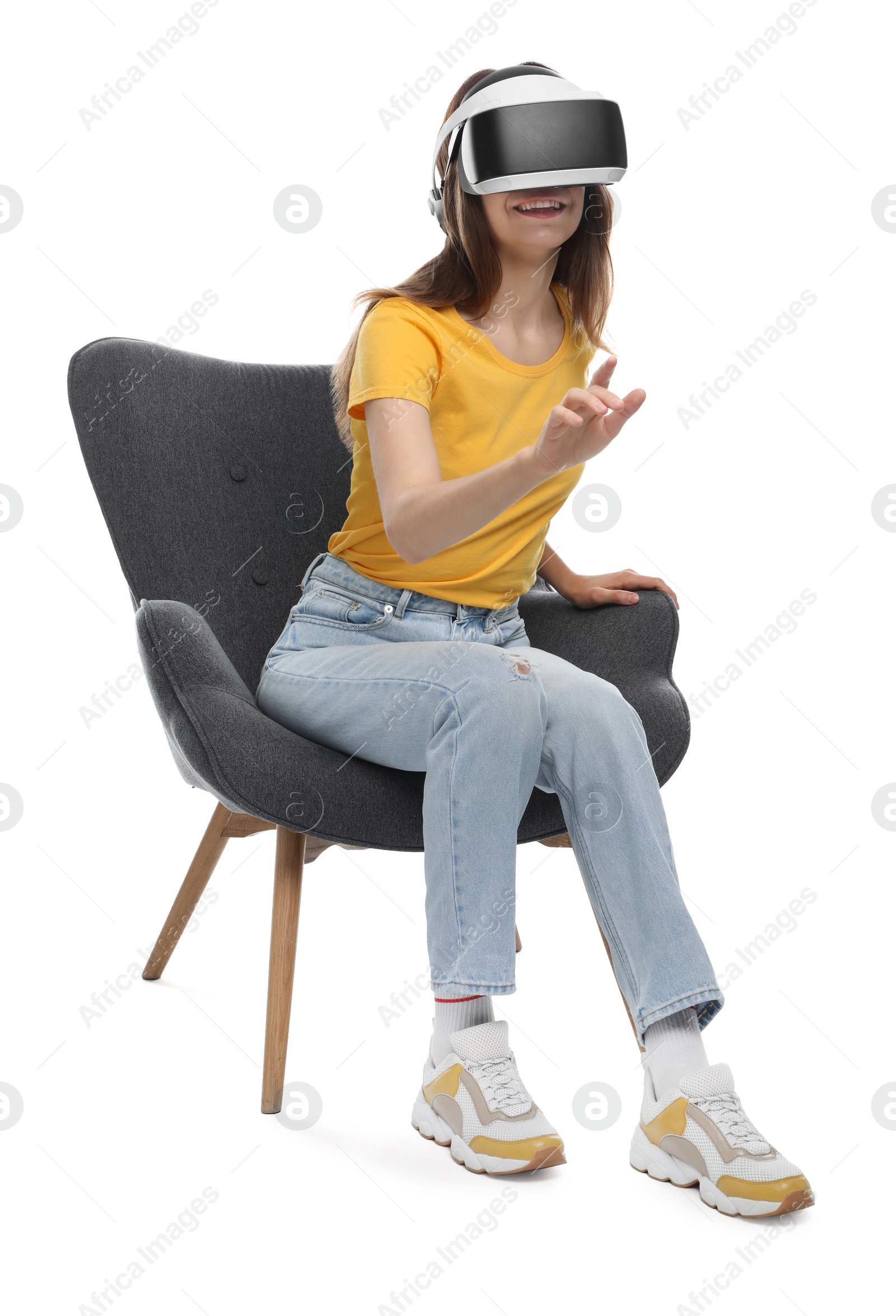 Photo of Smiling woman using virtual reality headset while sitting in armchair against white background