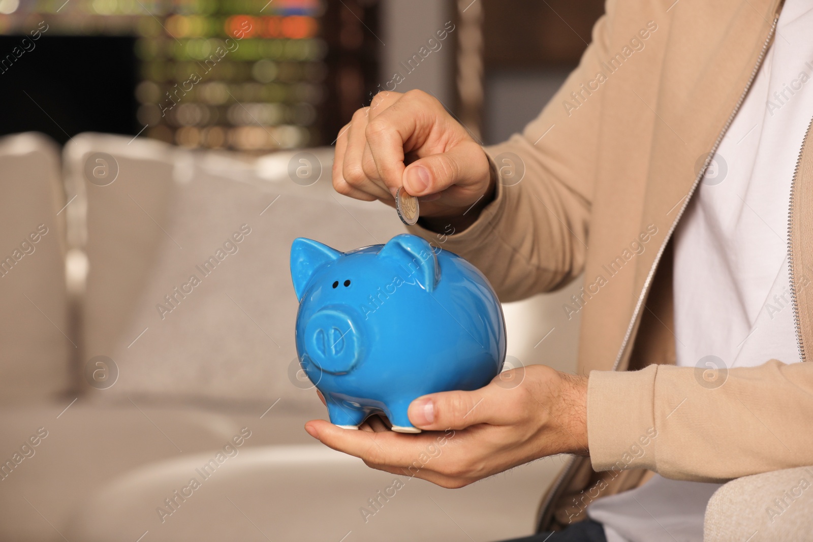 Photo of Man putting coin in piggy bank at home, closeup