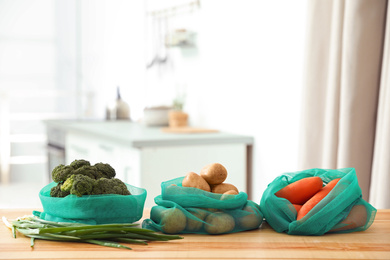 Net bags with vegetables on wooden table in kitchen