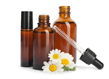 Chamomile flowers and cosmetic bottles of essential oil on white background