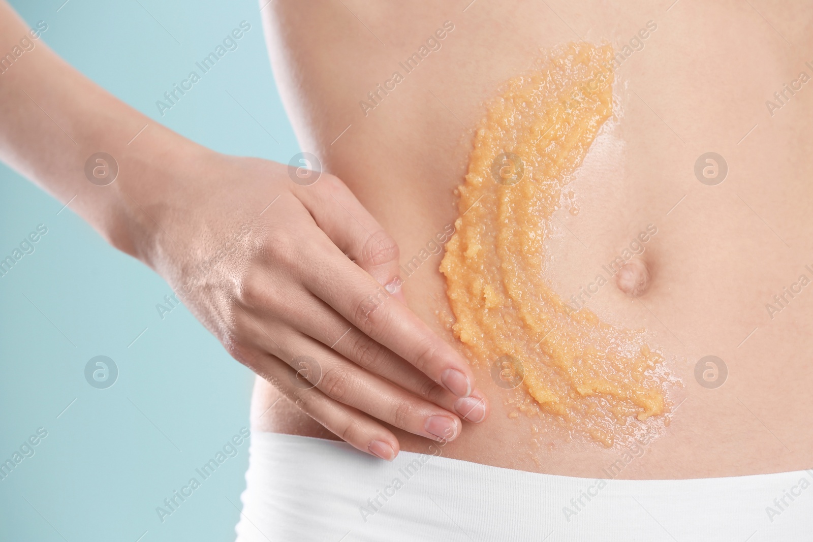 Photo of Young woman applying natural scrub on her belly against color background, closeup