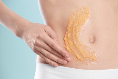 Young woman applying natural scrub on her belly against color background, closeup