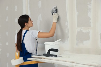 Worker plastering wall with putty knife indoors