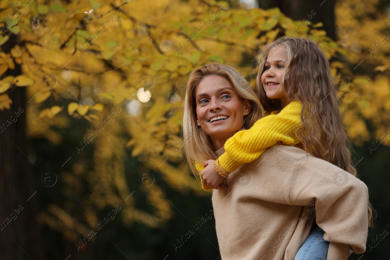 Photo of Portrait of happy mother and daughter in autumn park. Space for text