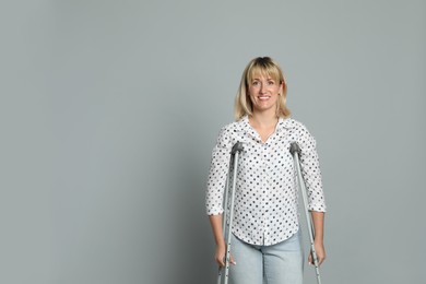 Photo of Portrait of happy woman with crutches on grey background. Space for text