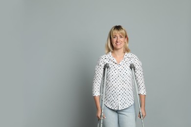 Portrait of happy woman with crutches on grey background. Space for text