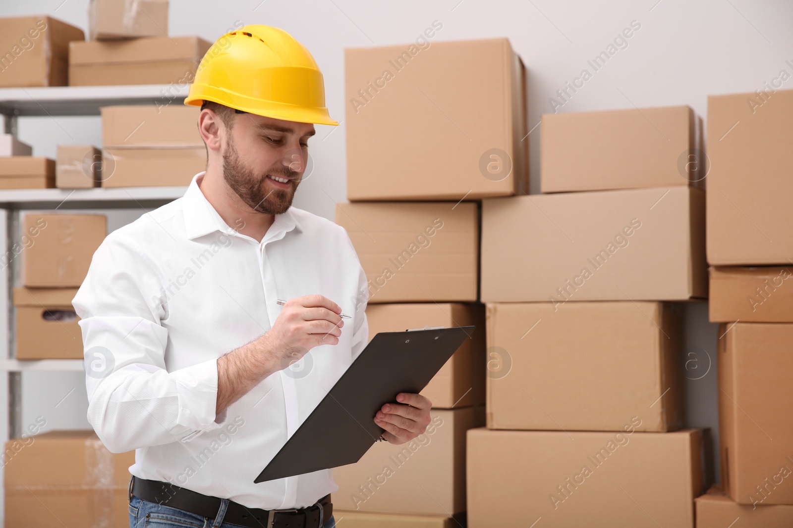 Photo of Young man with clipboard near cardboard boxes at warehouse