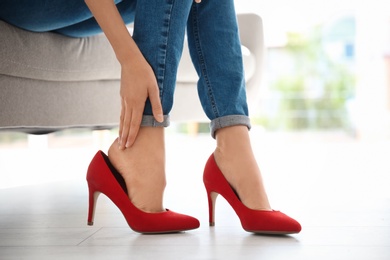 Tired woman with beautiful legs taking off shoes at home, closeup