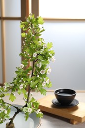 Stylish ikebana as house decor. Beautiful fresh branch with flowers and cup of tea on table, space for text