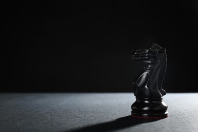 Photo of Black knight on table against dark background, space for text. Chess piece