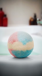 Photo of Colorful bath bomb on tub indoors. Spa product
