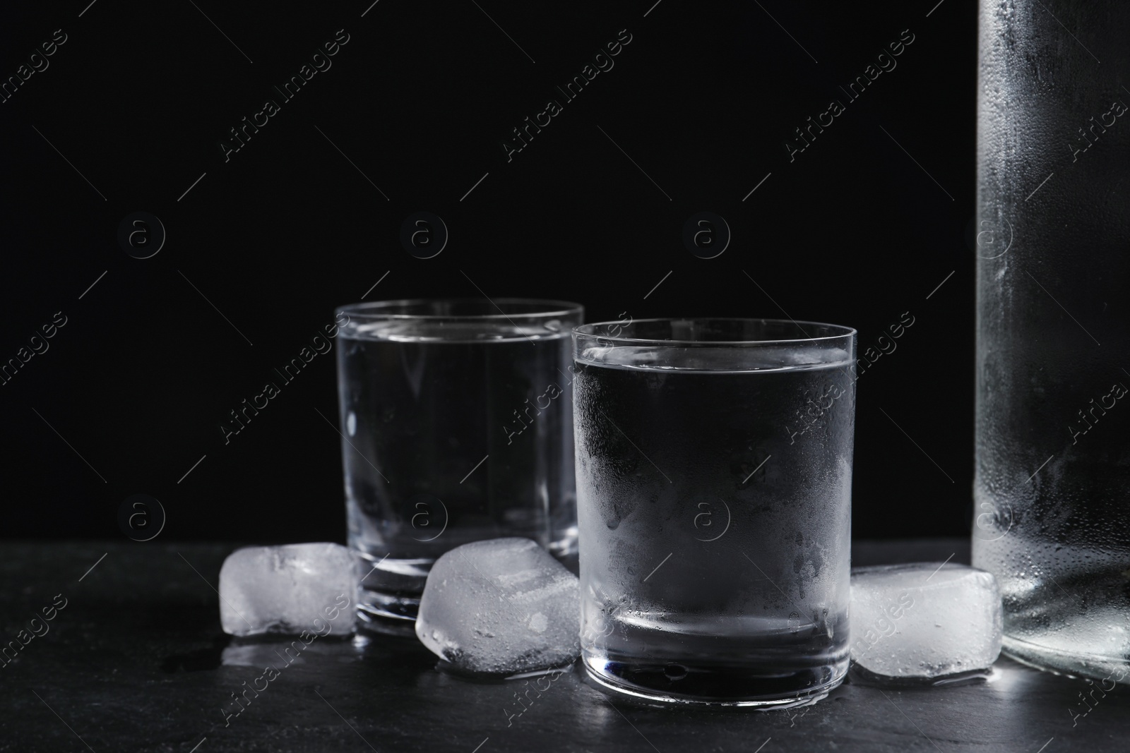 Photo of Vodka in shot glasses with ice on table against black background