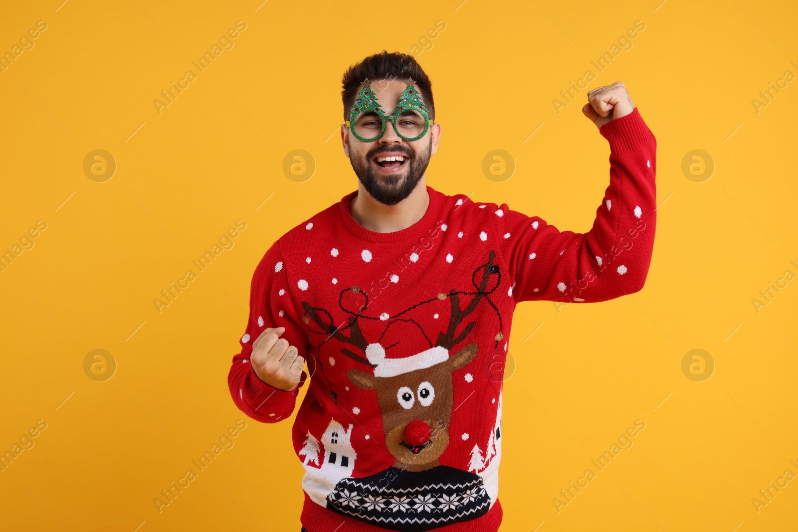 Photo of Happy young man in Christmas sweater and funny glasses on orange background