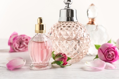 Photo of Different bottles of perfume and flowers on light background, closeup