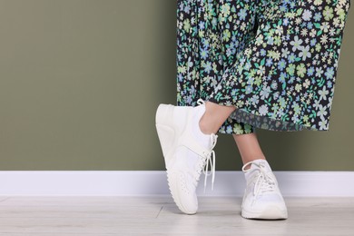 Photo of Woman wearing pair of new stylish sneakers near dark olive wall, closeup. Space for text