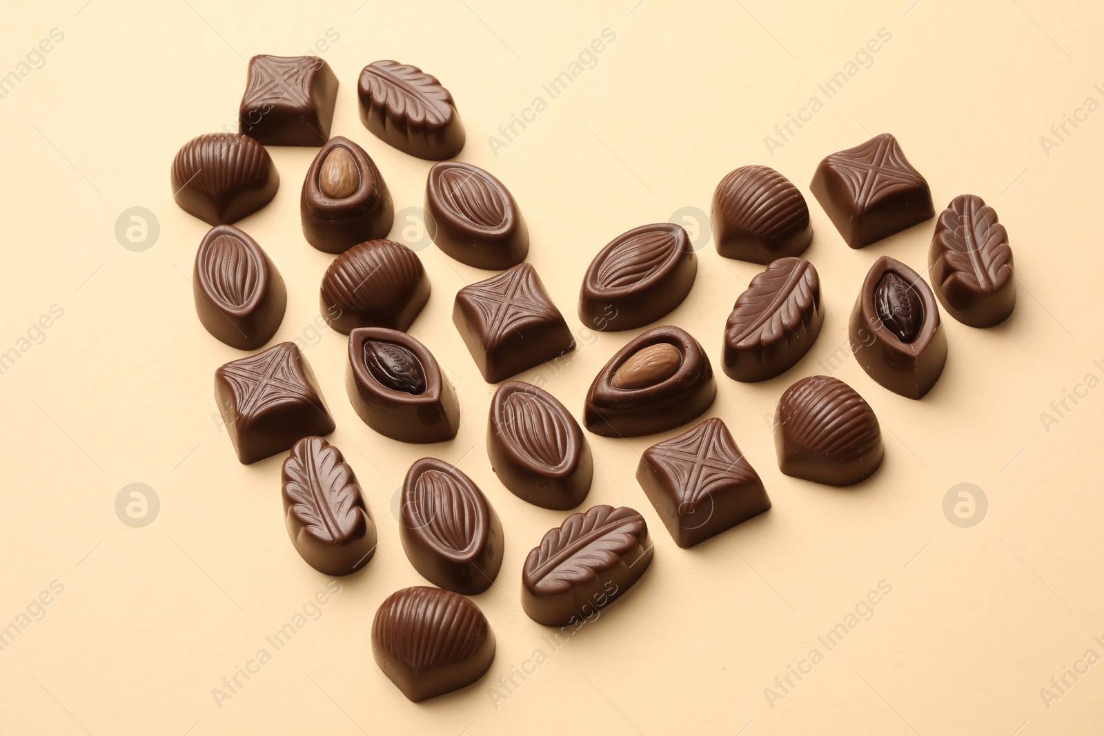 Photo of Heart made with delicious chocolate candies on beige background, above view