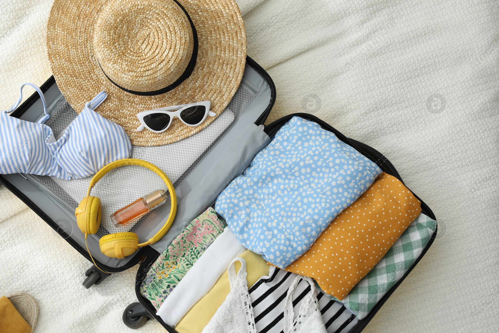 Photo of Open suitcase full of clothes and summer accessories on bed, flat lay