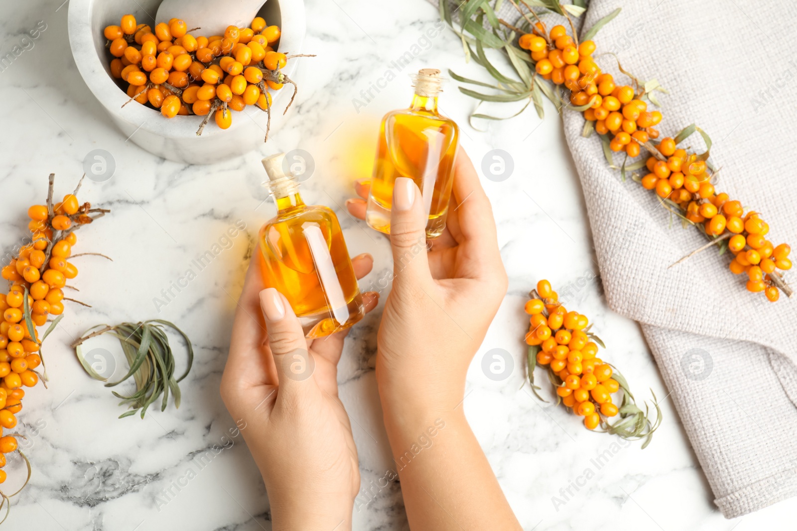 Photo of Woman holding bottles with natural sea buckthorn oil at white marble table, top view