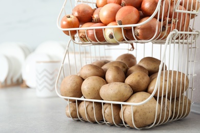 Photo of Container with potatoes and onions on grey kitchen counter. Orderly storage