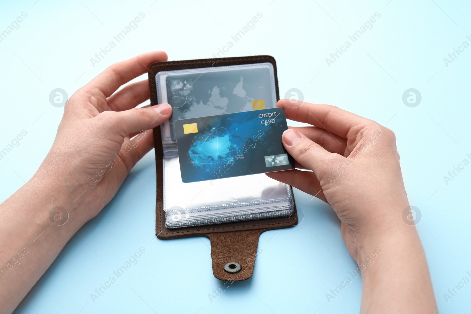 Photo of Woman holding leather card holder with credit cards on light blue background, closeup