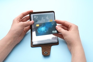 Woman holding leather card holder with credit cards on light blue background, closeup